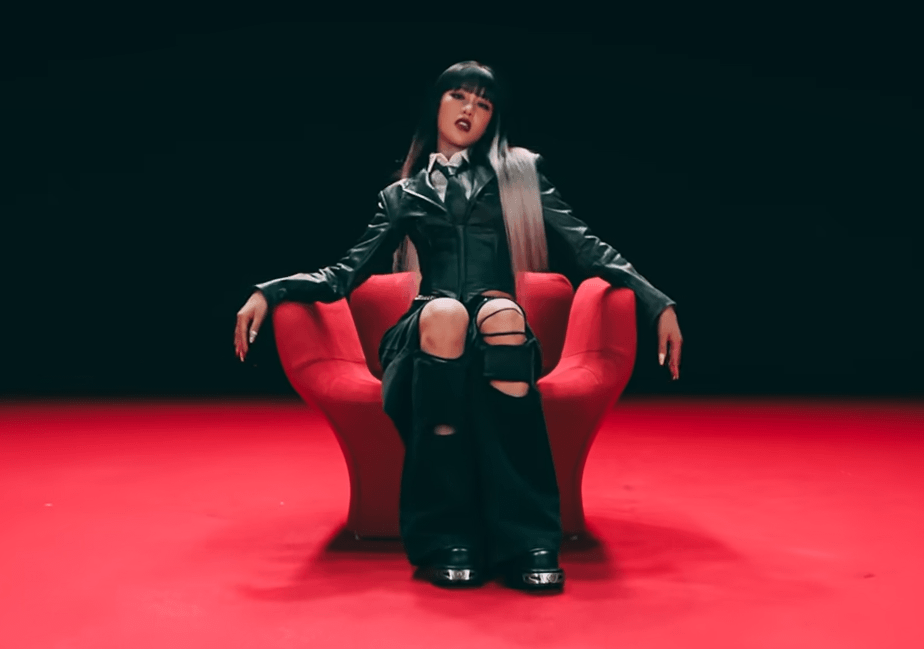 Minnie, assise sur une chaise rouge, porte une veste en (faux?) cuir avec un grand jean noir troué et des New Rock, des grosses bottes gothiques