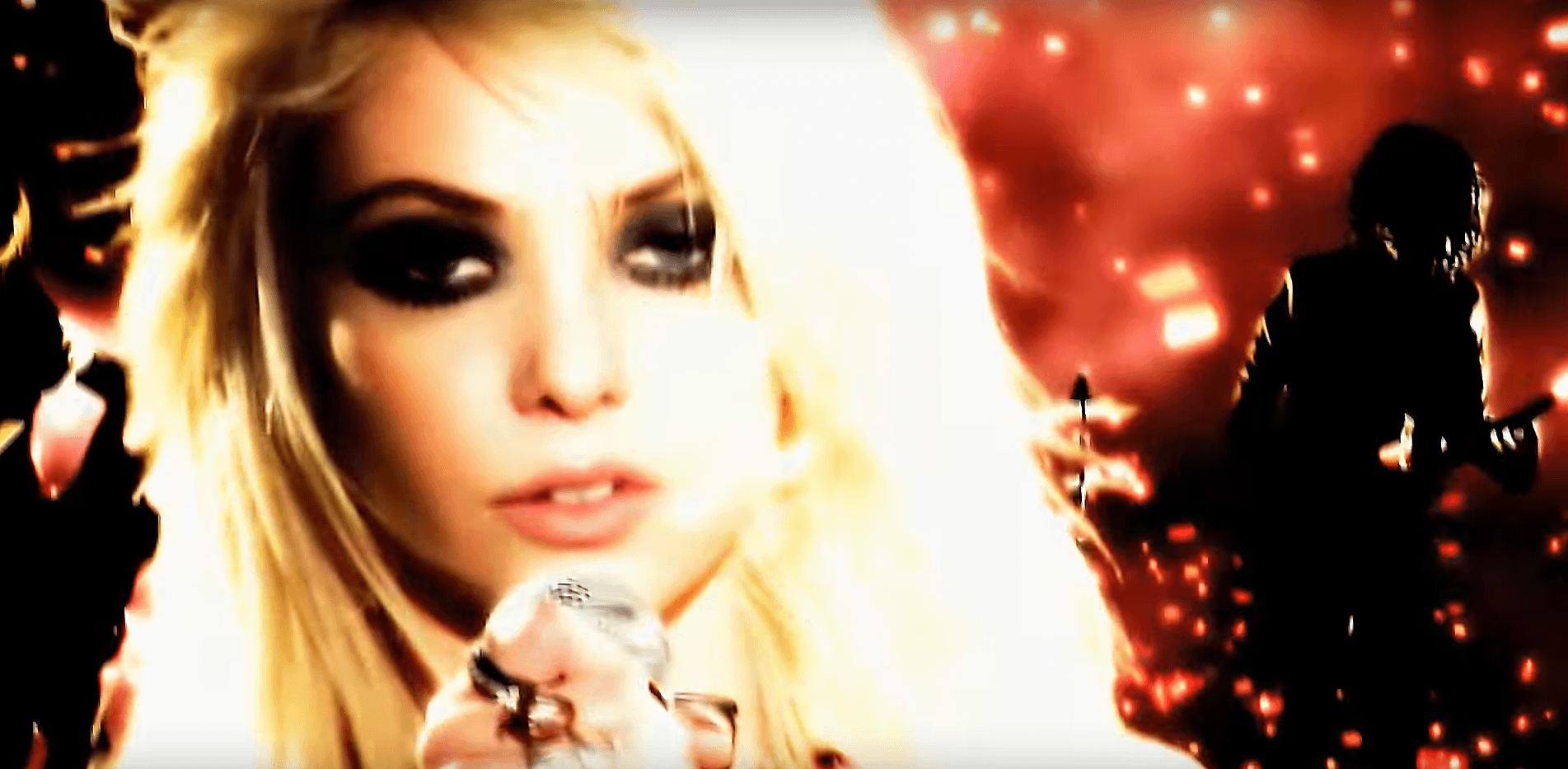 photo du clip Make Me Wanna Die de The Pretty Reckless, au premier plan Taylor Momsen, au second plan le guitariste, l'ambiance est rouge à cause du feu qui brûle derrière eux