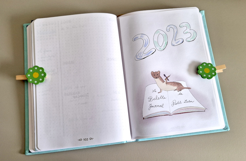 spreadpage for my 2023 setup in my bullet journal. on the right page, there's an illustration of a weasel above a notebook :it's a pun between the english 'bullet' and the french 'belette' because it sounds similar. I write 2023 above the illustration